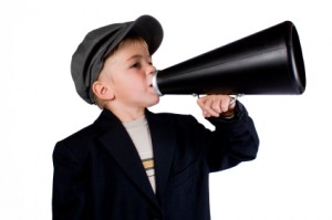 Little boy in a black jacket and hat talking into a black megaphone 